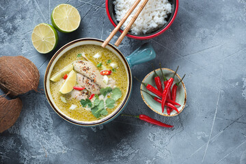 Top view of green curry with chicken, white rice, lime and red chili peppers, horizontal shot on a grey stone background
