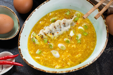 Green bowl of chinese traditional egg-drop soup with scallions and dumpling, close-up, elevated view