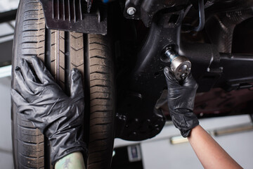 Cropped view of mechanic in gloves working with wrench near wheel of car in garage.