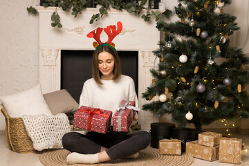 A surprised young girl sits and looks at two red Christmas gifts near the white fireplace