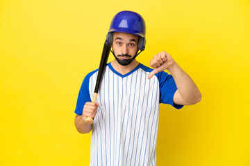 Young caucasian man playing baseball isolated on yellow background showing thumb down with negative expression