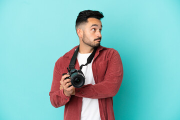 Young photographer caucasian man isolated on blue background making doubts gesture while lifting the shoulders