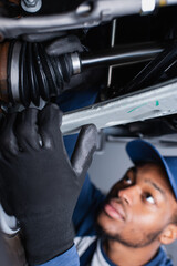 Blurred african american mechanic in gloves working with auto in garage.