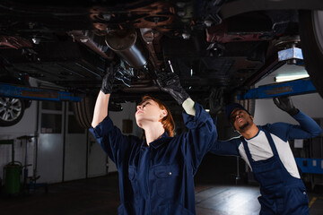 interracial technicians inspecting bottom of lifted auto in car service.