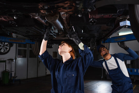 interracial technicians inspecting bottom of lifted auto in car service.