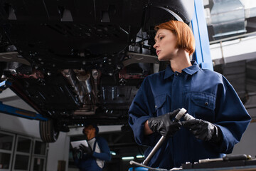 Low angle view of workwoman holding wrench near auto in garage.