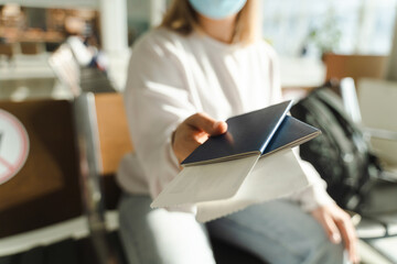 Woman in a mask sits in the waiting room and holds out her passport and ticket to the camera