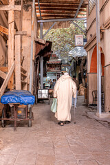 Naklejka premium Fes, Morocco. October 10, 2021. Rear view of senior old man walking with stick on street against restaurant
