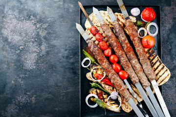Traditional Turk Adana kebap on shashlik skewer with barbecue vegetable and flatbread served as top view on a rustic metal tray with copy space left - obrazy, fototapety, plakaty