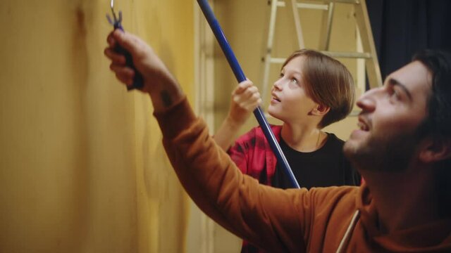 Father and son painting walls in yellow, making overhaul together with child. Doing renovating with kid and having fun. Interior design, new apartment. Boy helping to his parent.