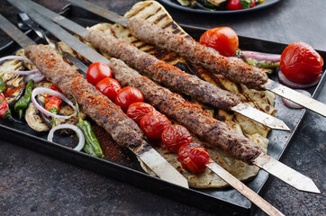 Traditional Turk Adana kebap on shashlik skewer with barbecue vegetable and flatbread served as close-up on a rustic metal tray