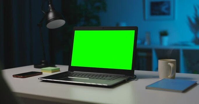 Over Shoulder View Of Woman Sitting At Living Room During Evening Time And Using Modern Computer. Focus On Portable Laptop With Chroma Key Screen That Standing On Table.