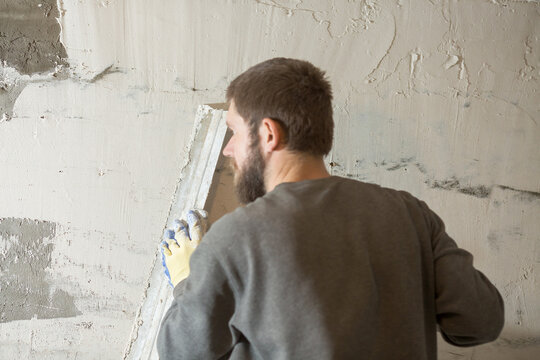a male plasterer with a beard plasters a concrete wall with a spatula.