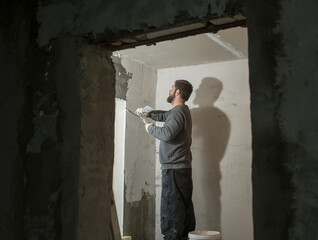 a male plasterer with a beard plasters a concrete wall with a spatula..