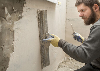 a man with a beard plasterer plasters a concrete wall under the windowsill with a spatula..