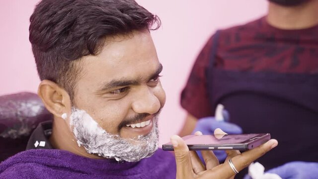 closeup shot of barber waiting for shave whille customer busy on phone call by using loudspeaker at salon - concept of tecnology, haircare service and samll business.