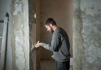 Obraz na płótnie Canvas a male plasterer with a beard plasters a concrete wall with a spatula..