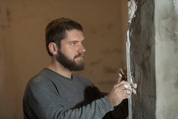 a man with a plasterer beard mounts a perforated painting corner on the corner of the doorway of...