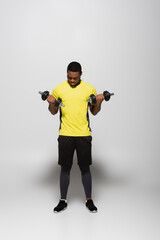 Fototapeta na wymiar full length of african american sportsman working out with dumbbells on grey.