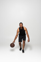 Fototapeta na wymiar full length of muscular african american man playing basketball on grey.