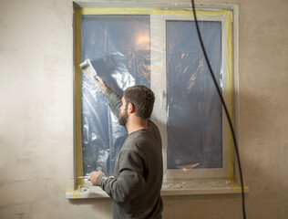 a man with a beard plasters window slopes with a spatula and putty...