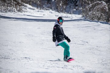 Fototapeta na wymiar a girl on a snowboard rides down the side of the mountain
