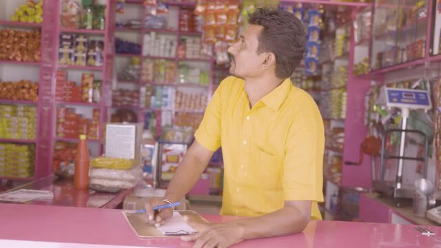 Kirana or groceries merchant or shopkeeper noting product list by looking around at shop for holiday festival sales- concept of professional occupation, successful small business.