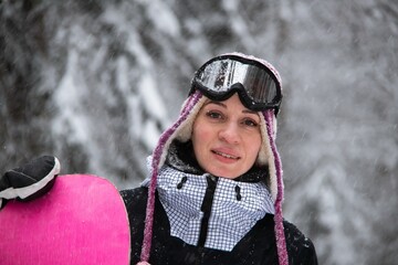 Girl with a snowboard in the forest in the mountains and the snowfall