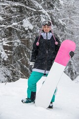 Girl with a snowboard in the forest in the mountains and the snowfall