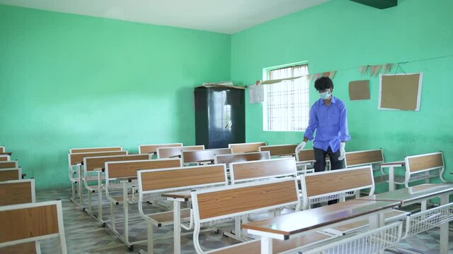 Wide angle shot, indian teacher rearrenging classroom desk or bench for social distance safety rules due to covid-19 pendamic at school - concept of back to school, prevention and protection from