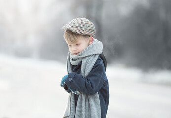 Obraz premium a boy in vintage clothes is standing by the road, he is cold, he is shivering, winter and snow, steam is coming out of his mouth.