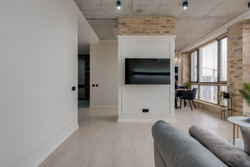 interior in a modern style and a view of the TV and part of the kitchen near the large windows with blinds