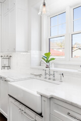 A luxurious, kitchen sink detail shot. The sink features a chrome faucet on a white apron sink in...