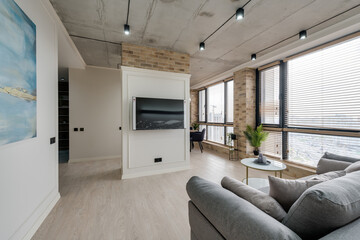 interior in a modern style and a view of the TV and part of the kitchen near the large windows with blinds