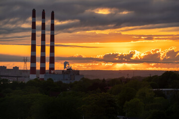 Naklejka premium Power plant smoke stacks silhouetted against a dramatic sunset.