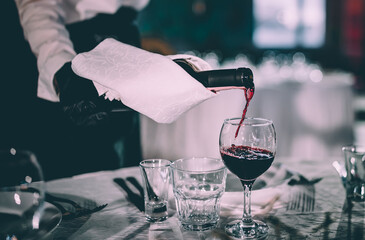 waiter pouring red wine into a glass in cafe or restaurant