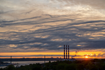 Power plant smoke stacks silhouetted against a dramatic sunset. - 477755135