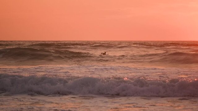 Close up on the waves and surfers at the sunset in slow-motion