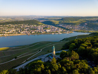 Fototapeta premium Luftaufnahme mit Drohne vom Niederwalddenkmal und Weinbergen in Richtung Bingen am Rhein während des Sonnenuntergangs an einem teilweise bewölkten Tag im Sommer, Rheingau Hessen 