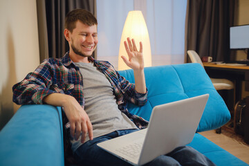 Man sitting on sofa and making video call. Handsome male hipster having Video Conference at home. Happy mature guy relaxing on couch while video calling using laptop at home.