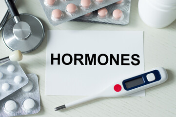 HORMONES word on a card on the table next to a thermometer, stethoscope and tablets