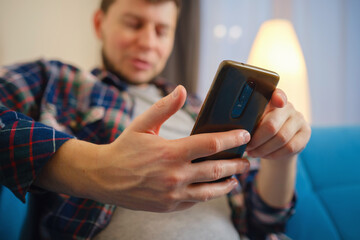 Happy man using mobile phone on a couch at home. Closeup of young man using smartphone to checking email at home, using app or social media