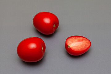red fresh tomatoes one of which is cut lie on a gray background