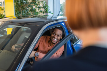 cheerful african american man looking at blurred car dealer while sitting in car.