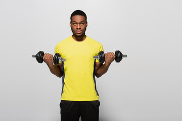 Fototapeta na wymiar young african american sportsman working out with dumbbells isolated on grey.