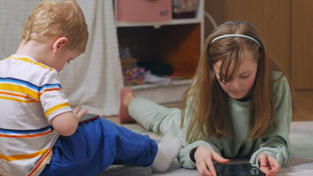 Brother and sister with gadgets sitting on the floor