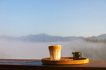 Sunrise coffee in nature. Dirty coffee on wooden table with mountain fog on shade of sunrise background. Good morning.