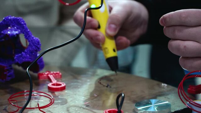 young white man draws 3d with a pen. excursion to the 3D printing factory. The yellow handle squeezes out the red plastic
