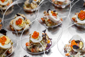 Light meat appetizer and chicken egg with red caviar and herbs in transparent cups on the table.