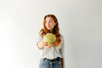 Selective focus on apple, portrait of a beautiful young woman with red wavy hair in a striped shirt...